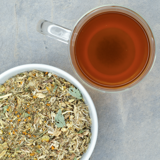 Tea leaves in a bowl with a cup of brewed tea on a gray surface
