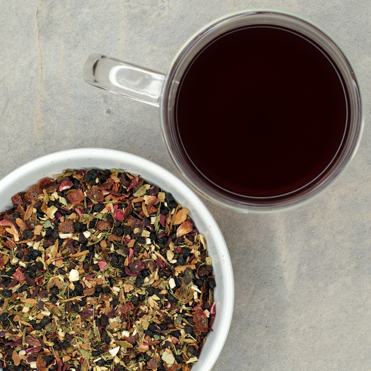 Clear mug of purple elderberry echinacea herbal tea next to a bowl of colorful loose herbal tea