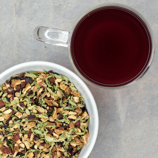 Tea leaves in a bowl with a cup of brewed tea on a gray surface