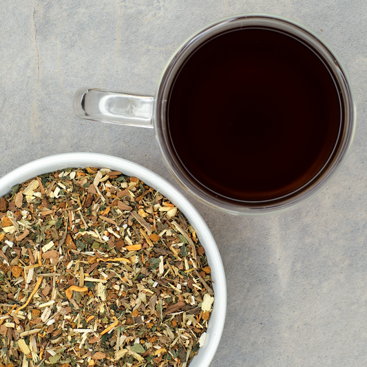 Herbal tea leaves in a bowl with a cup of brewed tea on a gray surface