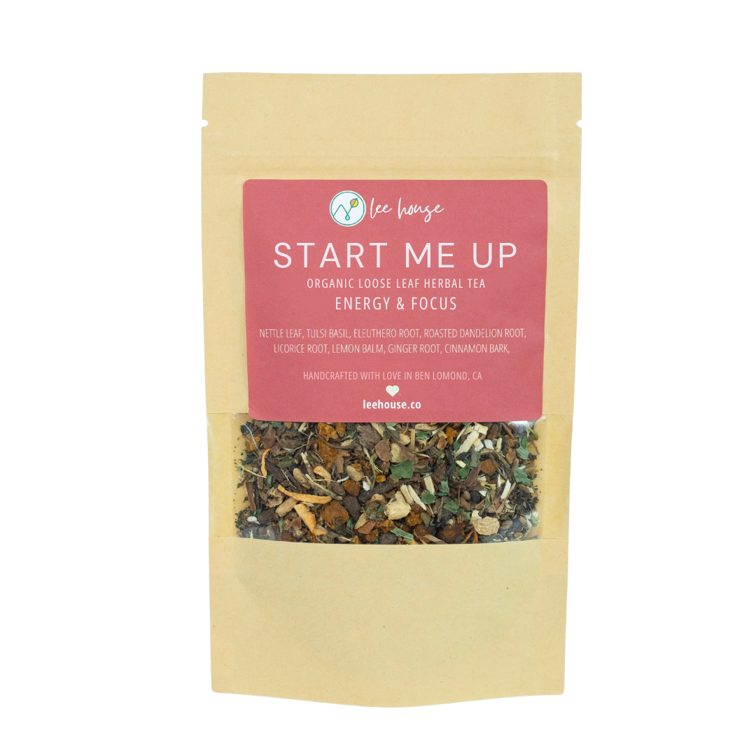 A stand-up pouch of Lee House 'Start Me Up' organic loose leaf herbal tea on a plain white background. The pouch is a light tan kraft paper color with a large pink label on the front and a clear window showing the loose leaf blend inside.