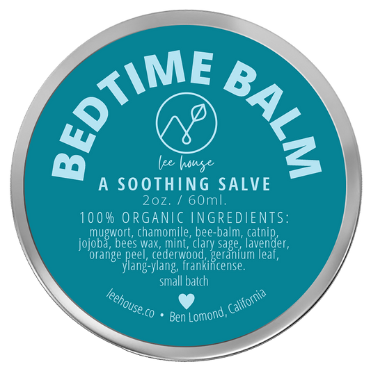 photograph of Bedtme Balm - photo contains a tin of slave with a bright blue label that reads: Bedtime Balm - all natural soothing salve. 100% organic: mugwort, chamomile, bee balm, catnip, jojoba, clary sage, mint, lavendar, orage peel, cedarwood, geranium leaf, ylnag ylang, frankincense, external use only. handcrafted sith love. leehouse.co