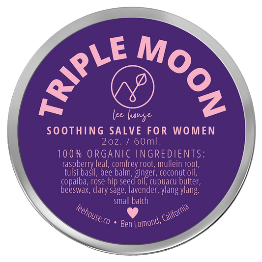 photo of a 2 oz tin of triple moon soothing balm for women depciting a purple and pin label that reads: 100% organic ingredients: raspberry Leaf, comfrey root, mullein root, tulsi basil, bee balm, ginger, coconut oil, copaiba, rose hip seed oil, cupuacu butter, beeswax, clary sage, lavender, ylang ylang. External Use Only. handcrafted with love, leehouse.co